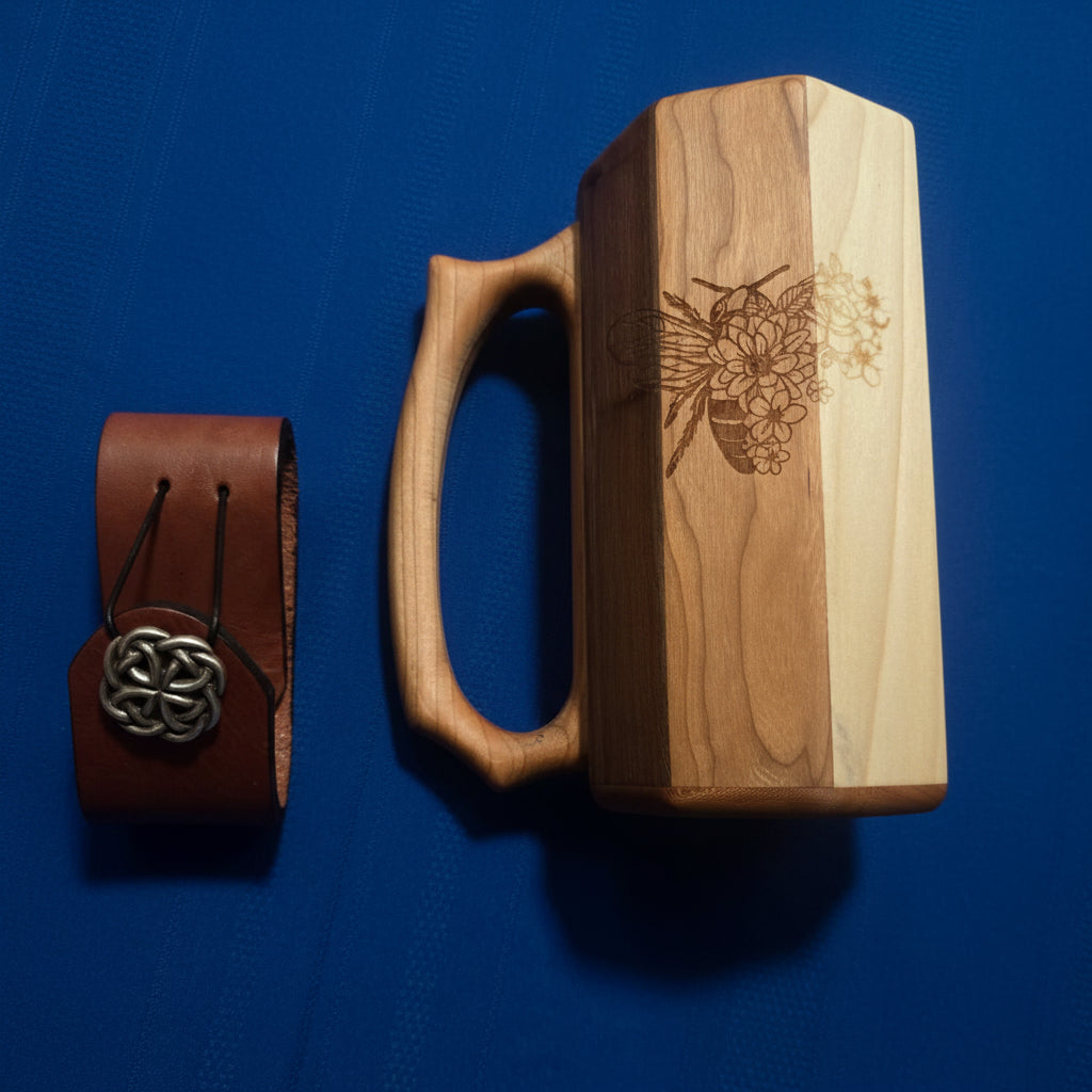 Wooden tankard with laser-engraved bee and floral design, shown alongside a leather mug strap with Celtic concho